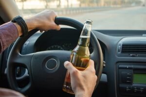 Man drinking beer while driving a car, illustrating the concept of not drinking and driving.