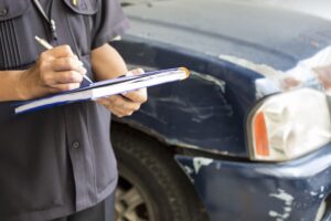 Side view of an insurance agent writing on paper while examining a car after an accident.