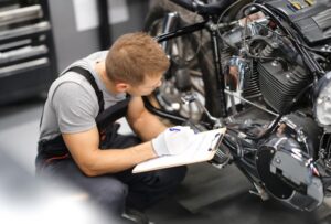 A mechanic inspecting a motorcycle and writing notes on a clipboard.