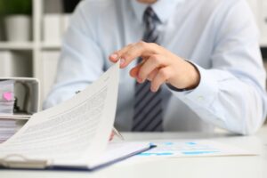 A person in a suit reading and handling documents at a desk.