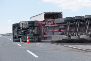 An overturned truck on the road with a traffic cone placed nearby for safety.