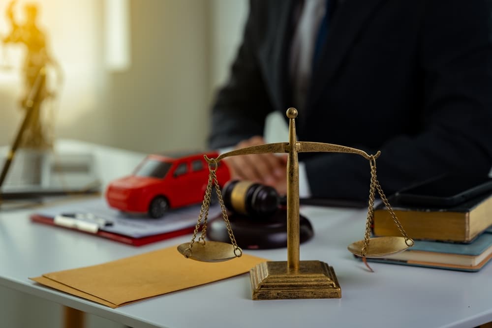 Scales of justice on a desk with a lawyer and car model.