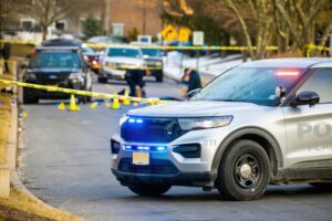 Police vehicles and officers at a cordoned-off crime scene with evidence markers.