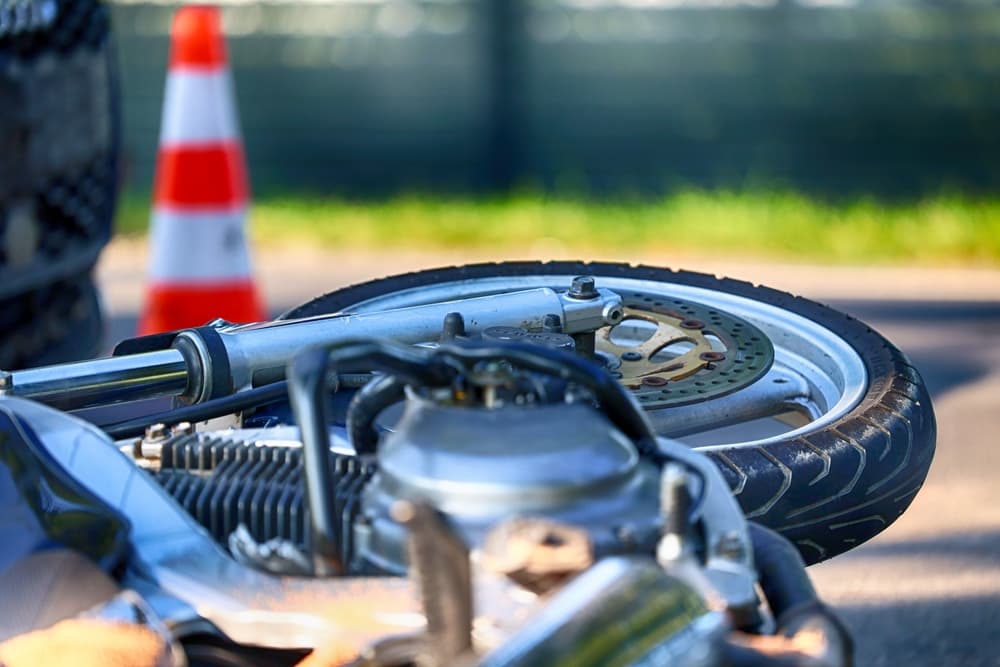 A close-up of a fallen motorcycle on the road near a traffic cone.