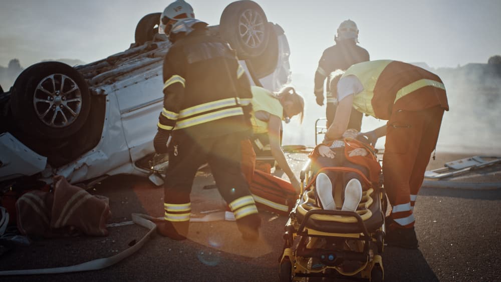 Emergency responders assist injured person at the scene of an overturned car accident.