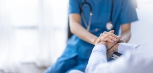 A medical professional in scrubs holding the hand of a patient, offering comfort during a consultation.