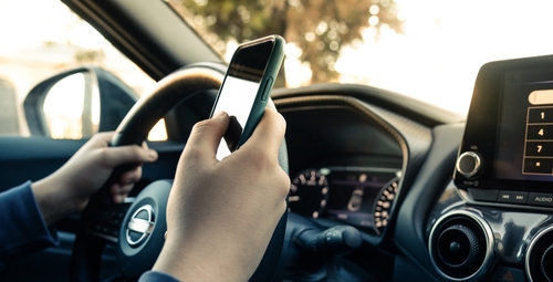 A driver holding a smartphone while driving, representing distracted driving caused by mobile phone use.