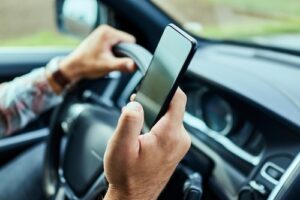 A close-up of a driver holding a smartphone while steering the car, exemplifying distracted driving.