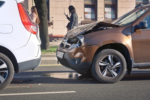 Two vehicles involved in a rear-end collision, with the front car's bumper and rear car's front end visibly damaged.