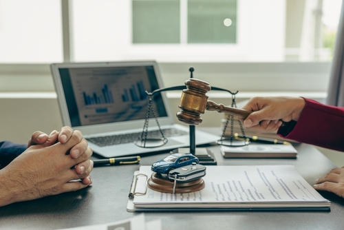 A lawyer holds a gavel over a model car, with legal documents and a laptop in the background, symbolizing car accident cases and legal proceedings.