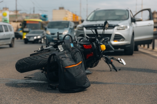 A motorcycle lying on the road after a collision with an SUV, with traffic in the background.