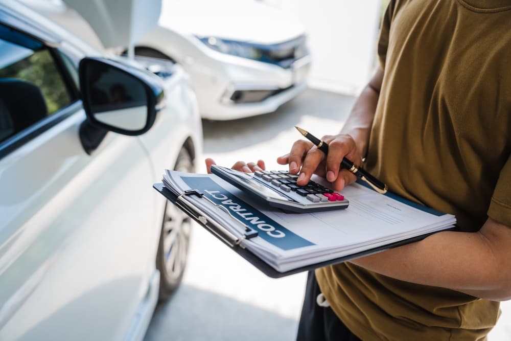 Man filling out a car insurance form after an accident, discussing coverage and deductible with an adjuster.