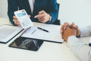 Young insurance agent pointing to a contract while sitting at a desk with a client in an office setting.